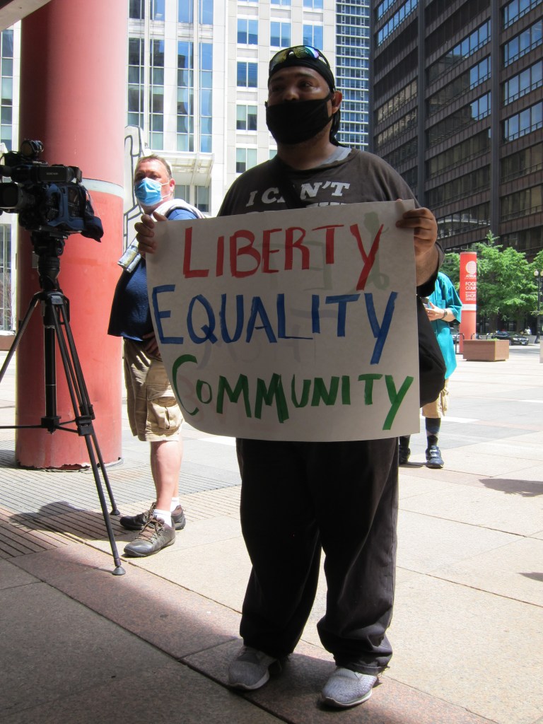 A person is holding a sign reading "Liberty, Equality, Community"